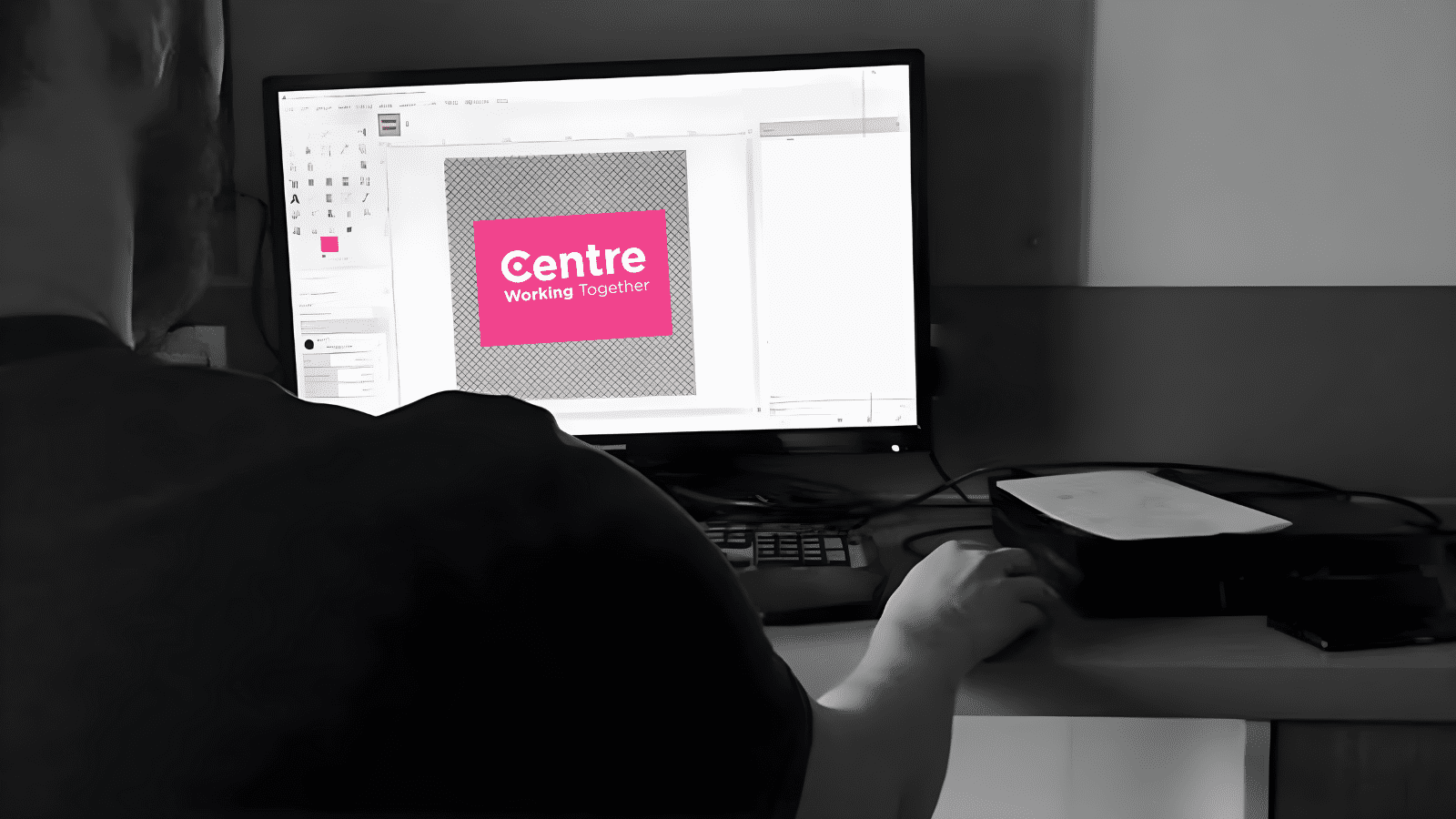Laptop screen with the Centre Think Tank logo in pink on it. A person is sitting in front of the laptop with their hand on a mouse. Other than the logo, the rest of the image is in black and grey.